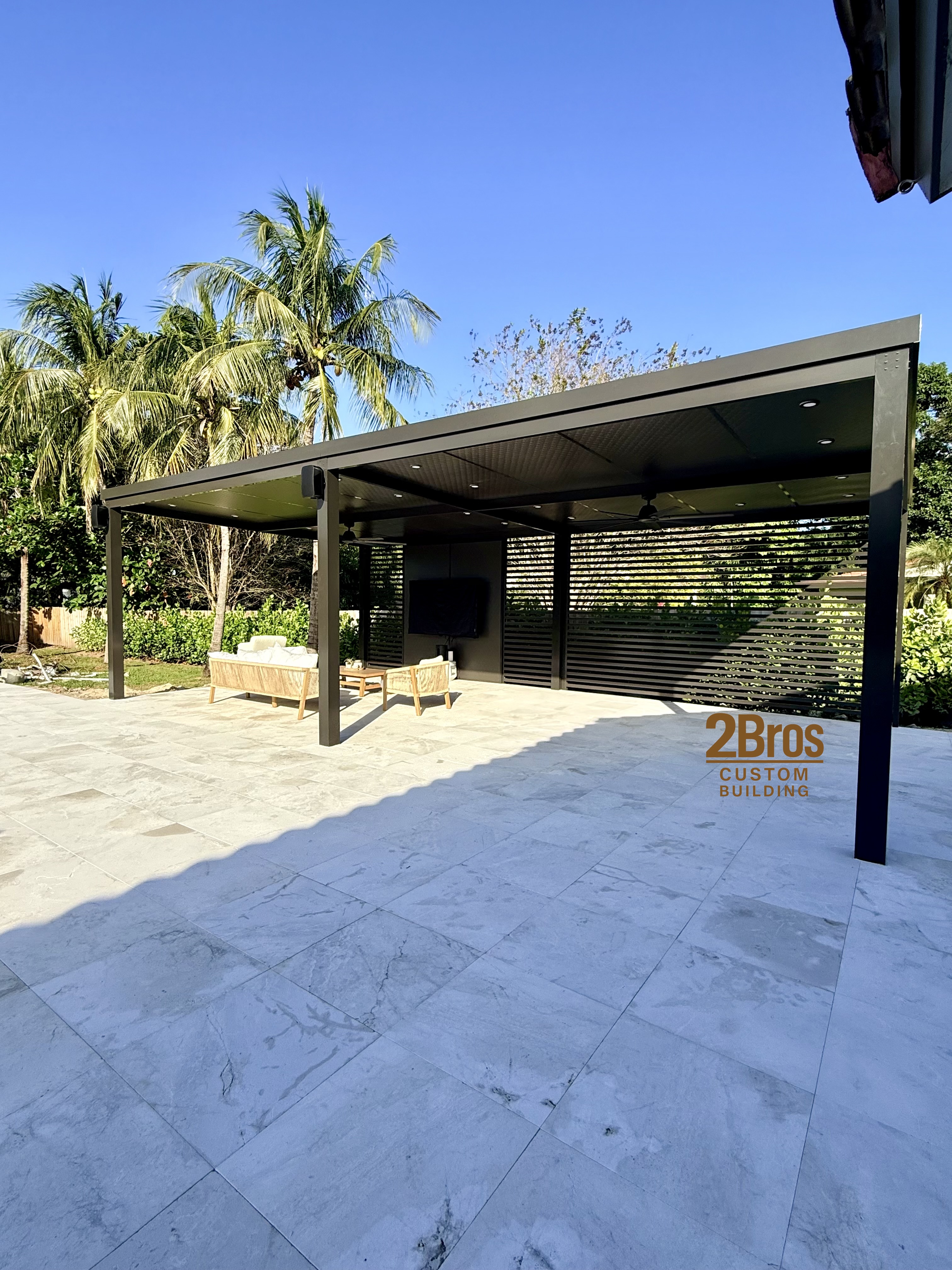 Dark charcoal freestanding pergola with outdoor lounge furniture and palm trees