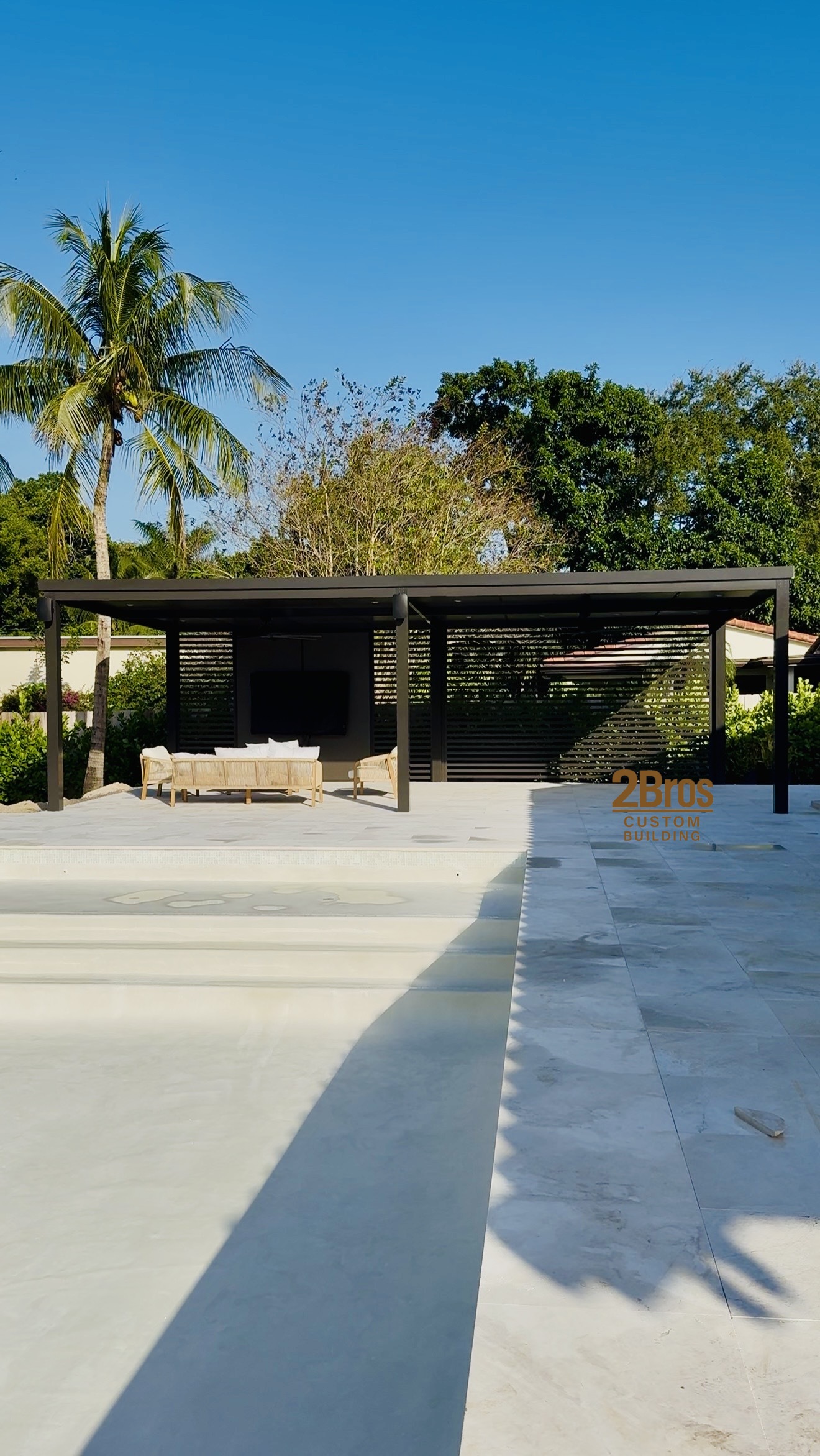 Dark pergola adjacent to pool with marble deck and tropical landscape